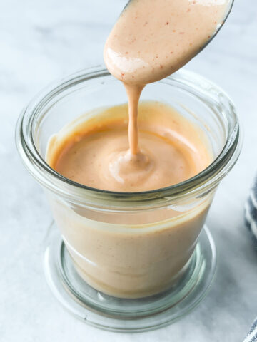 Spoonful of spicy mayo flowing from a spoon over a jar.