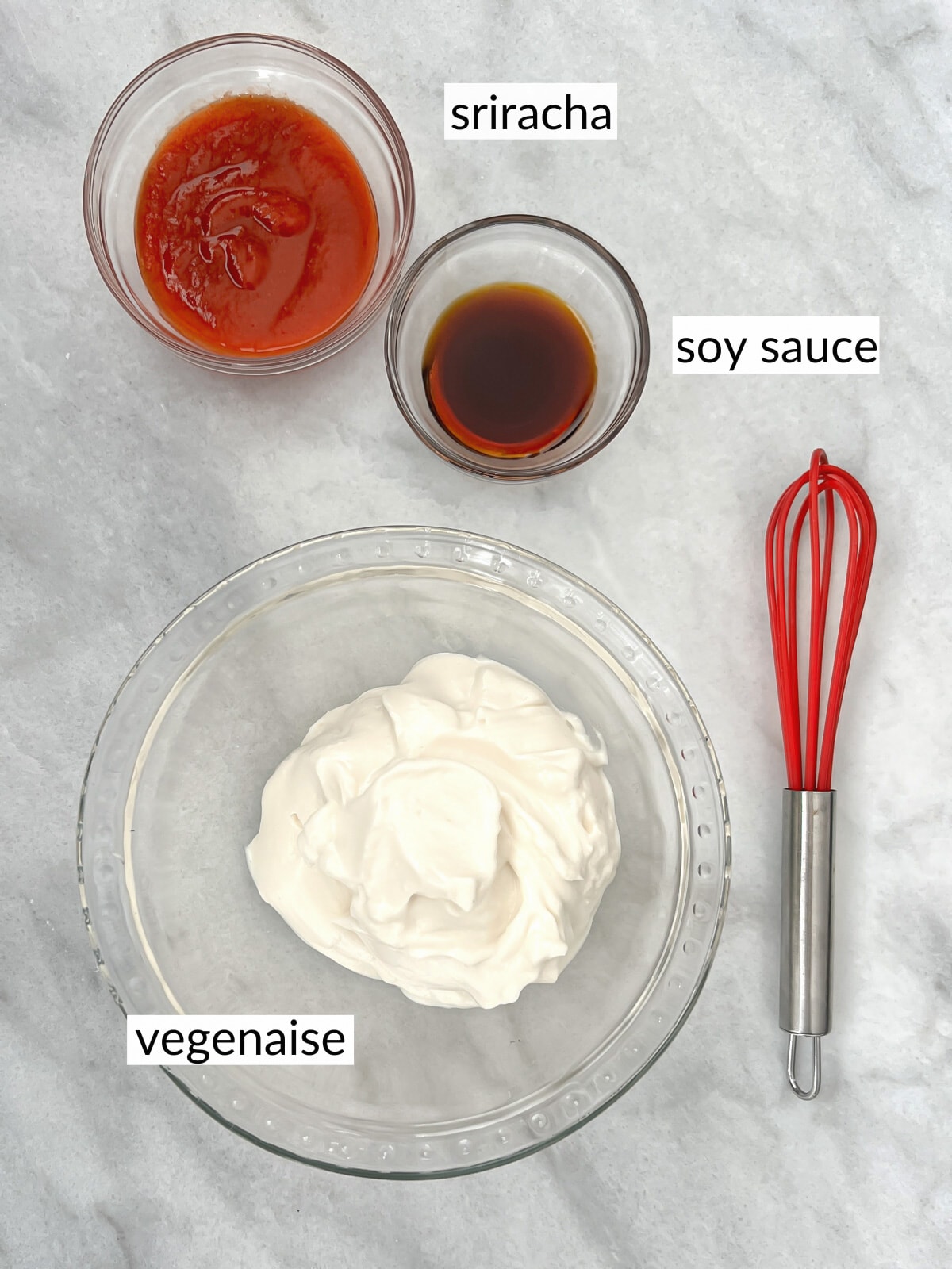 Ingredients for spicy mayo with a whisk laid out on white marble counter top.