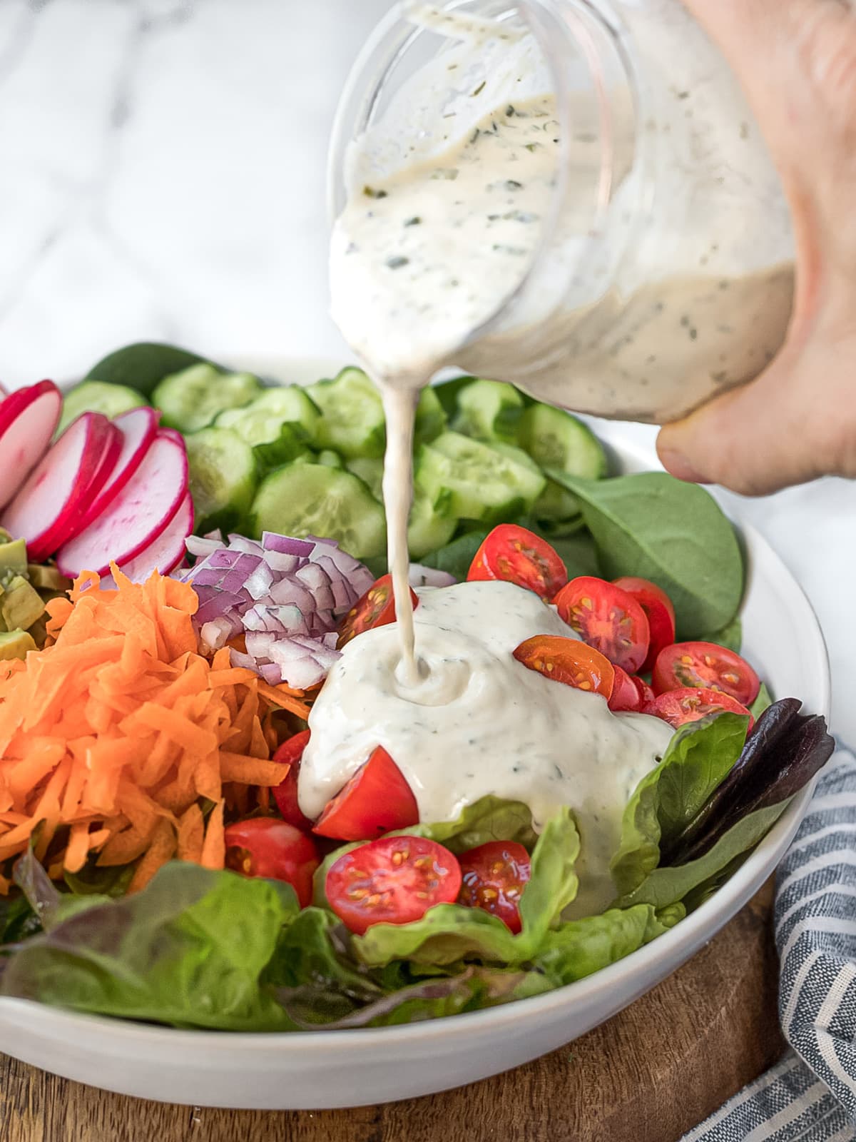 Ranch dressing being poured onto a garden salad.