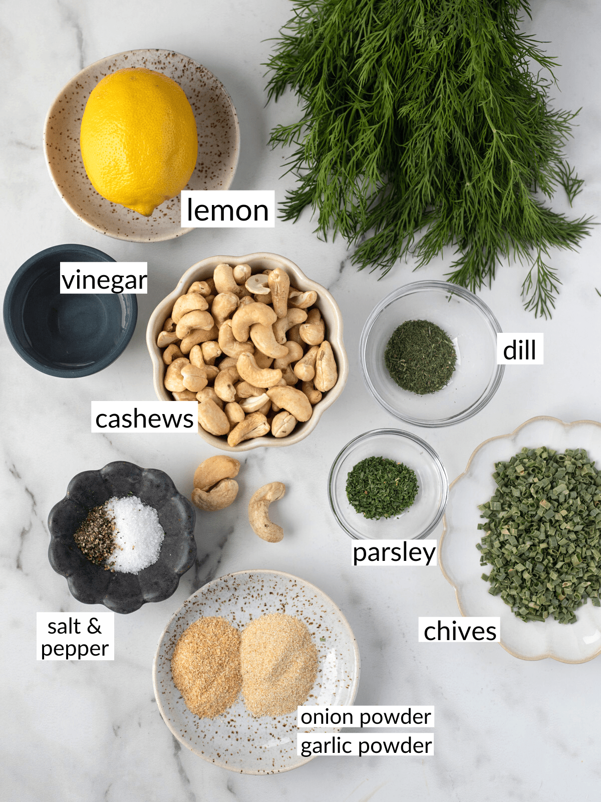 Ingredients for vegan ranch dressing in bowls on a white countertop including fresh dill and cashews.