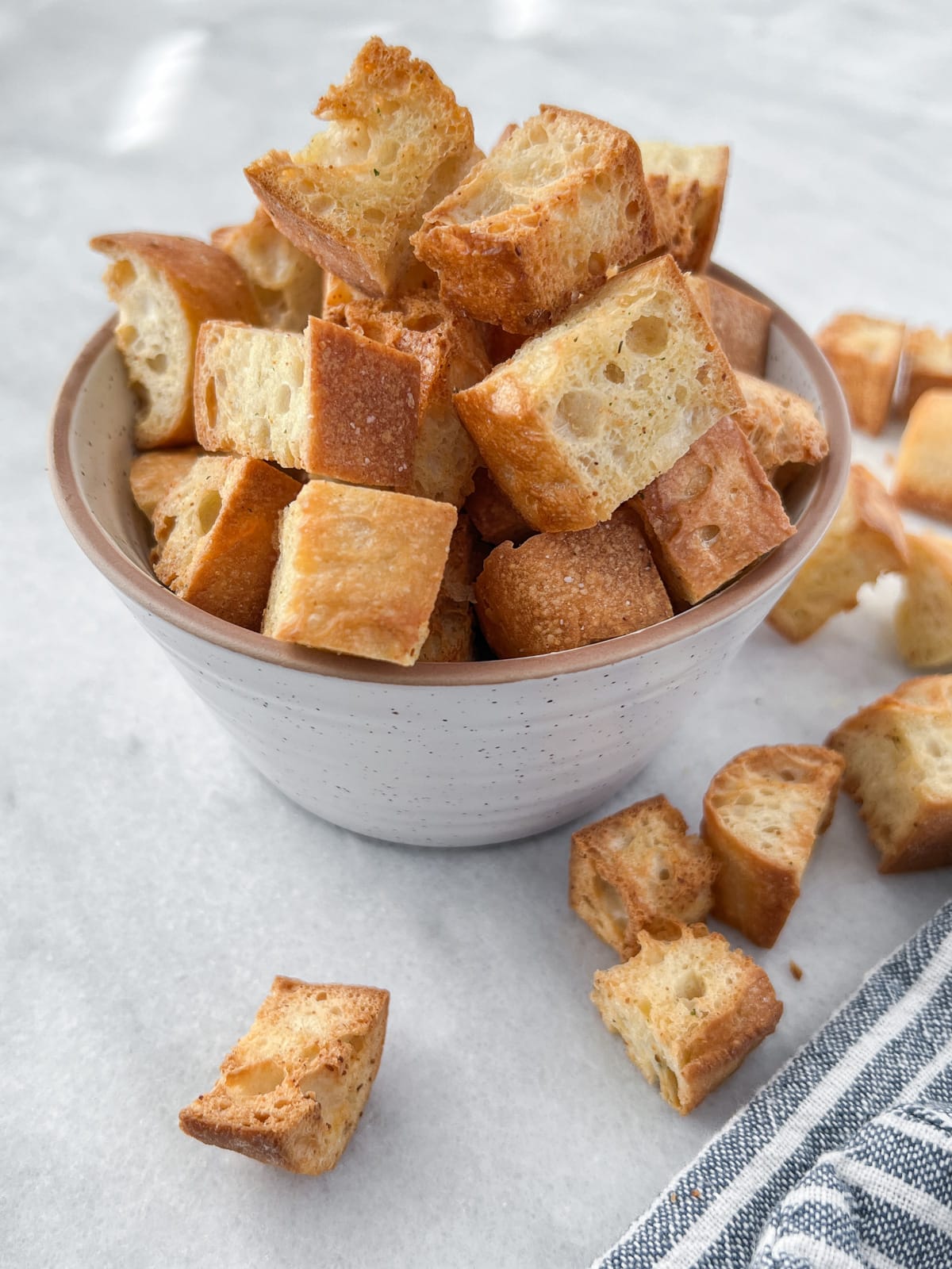 Bowlful of crispy croutons spilling out onto the countertop.