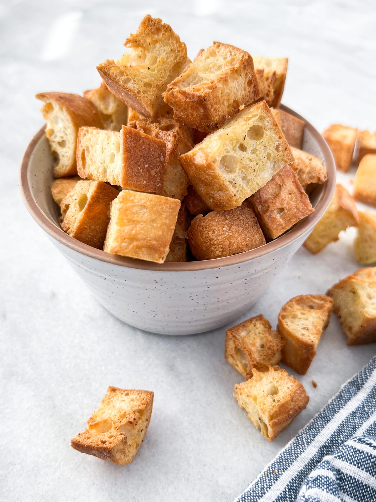 Overflowing bowl of crispy golden brown croutons on a white countertop.