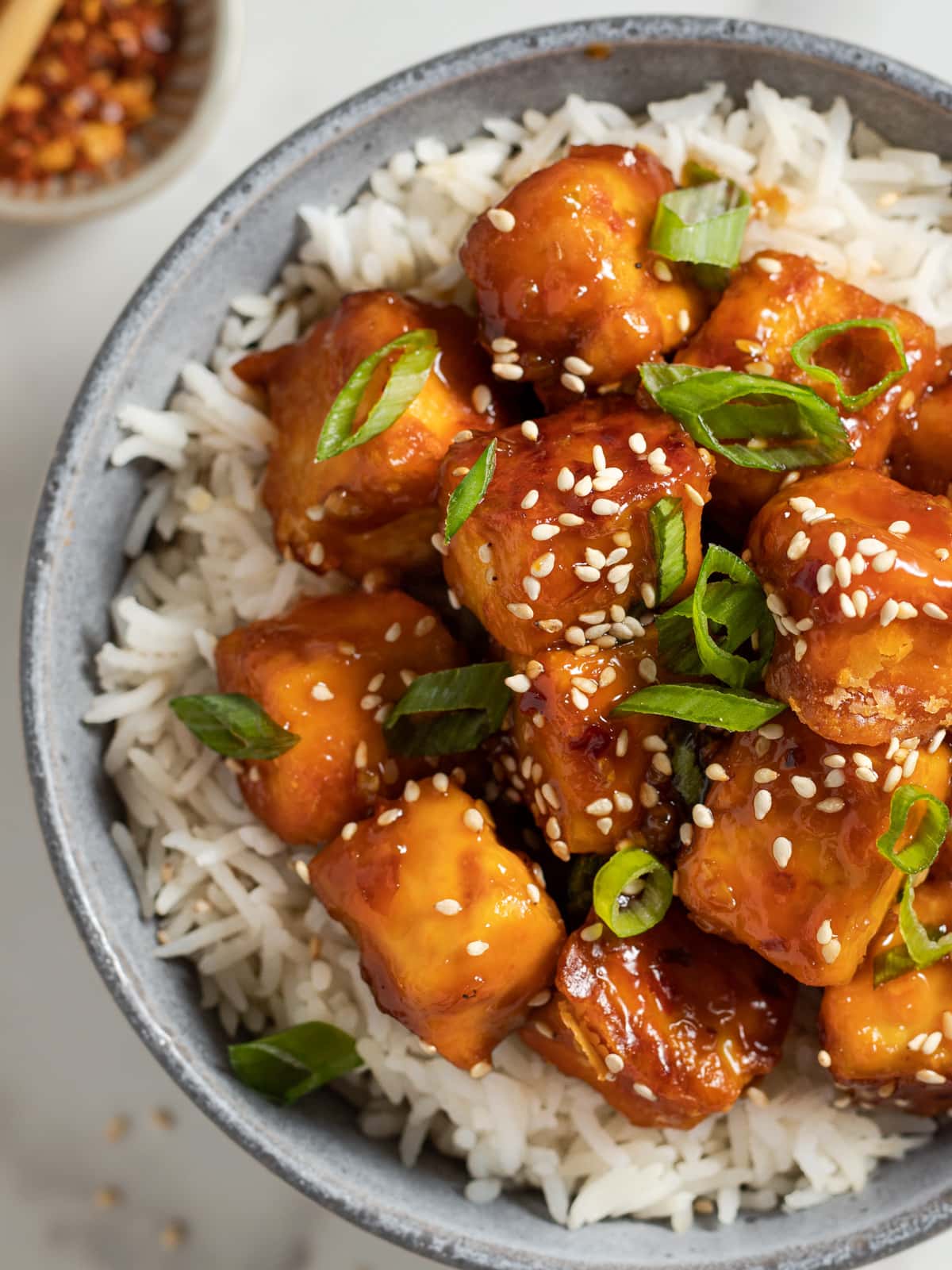Bowlful of teriyaki tofu on a bed of rice topped with sesame seeds and green onions.