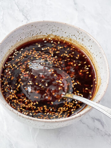 Spoonful of sesame seed teriyaki sauce being lifted from a white bowl.