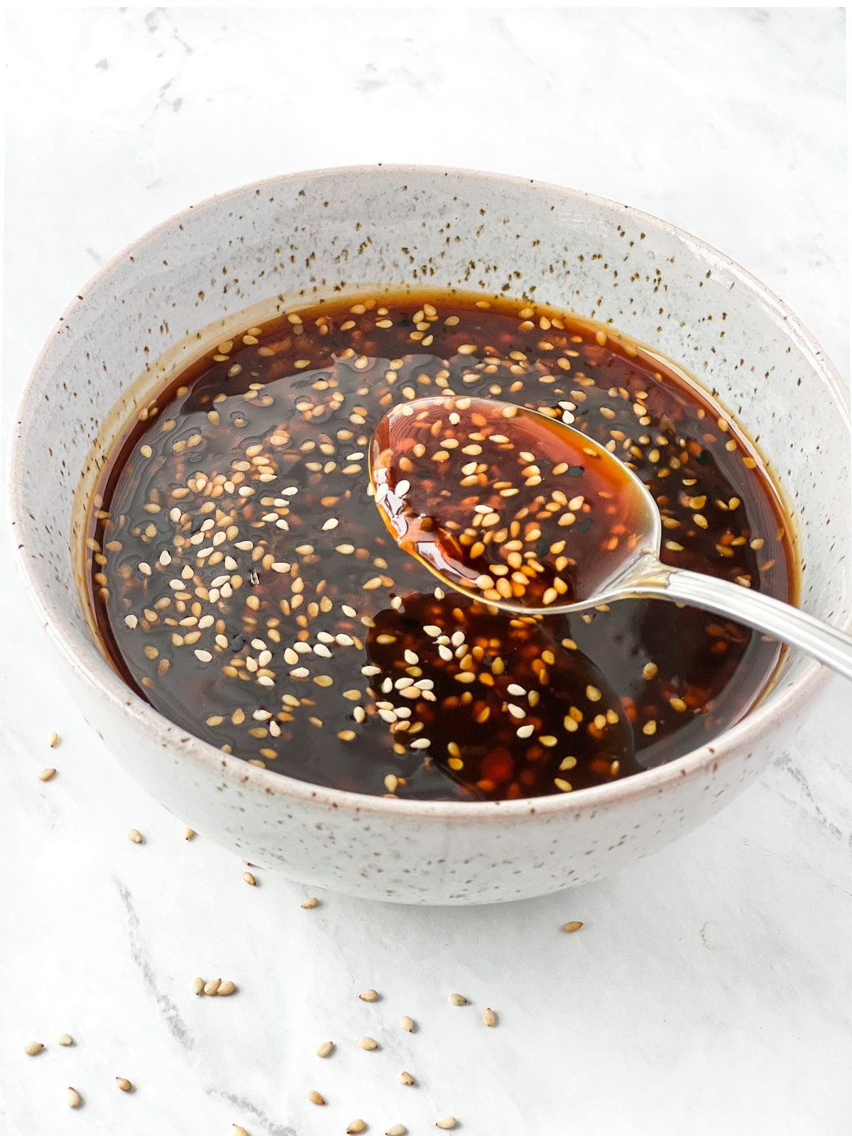 Spoonful of sesame seed topped teriyaki sauce being lifted out of bowl.