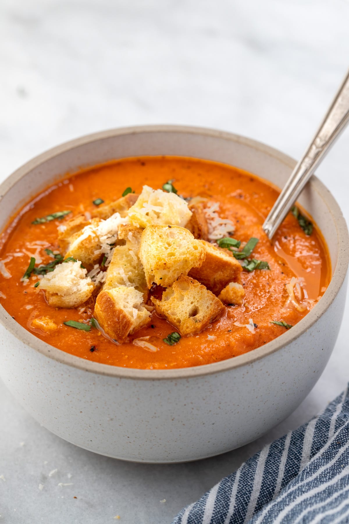 Bowl of dairy-free tomato soup topped with a pile of croutons and a sprinkle of grated cheese.