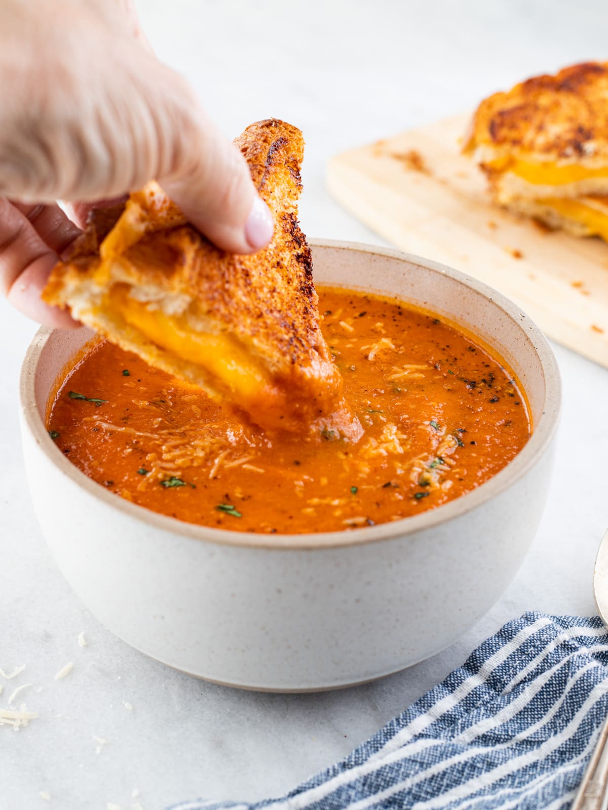 Grilled cheese sandwich being dipped into a bowl of tomato soup.