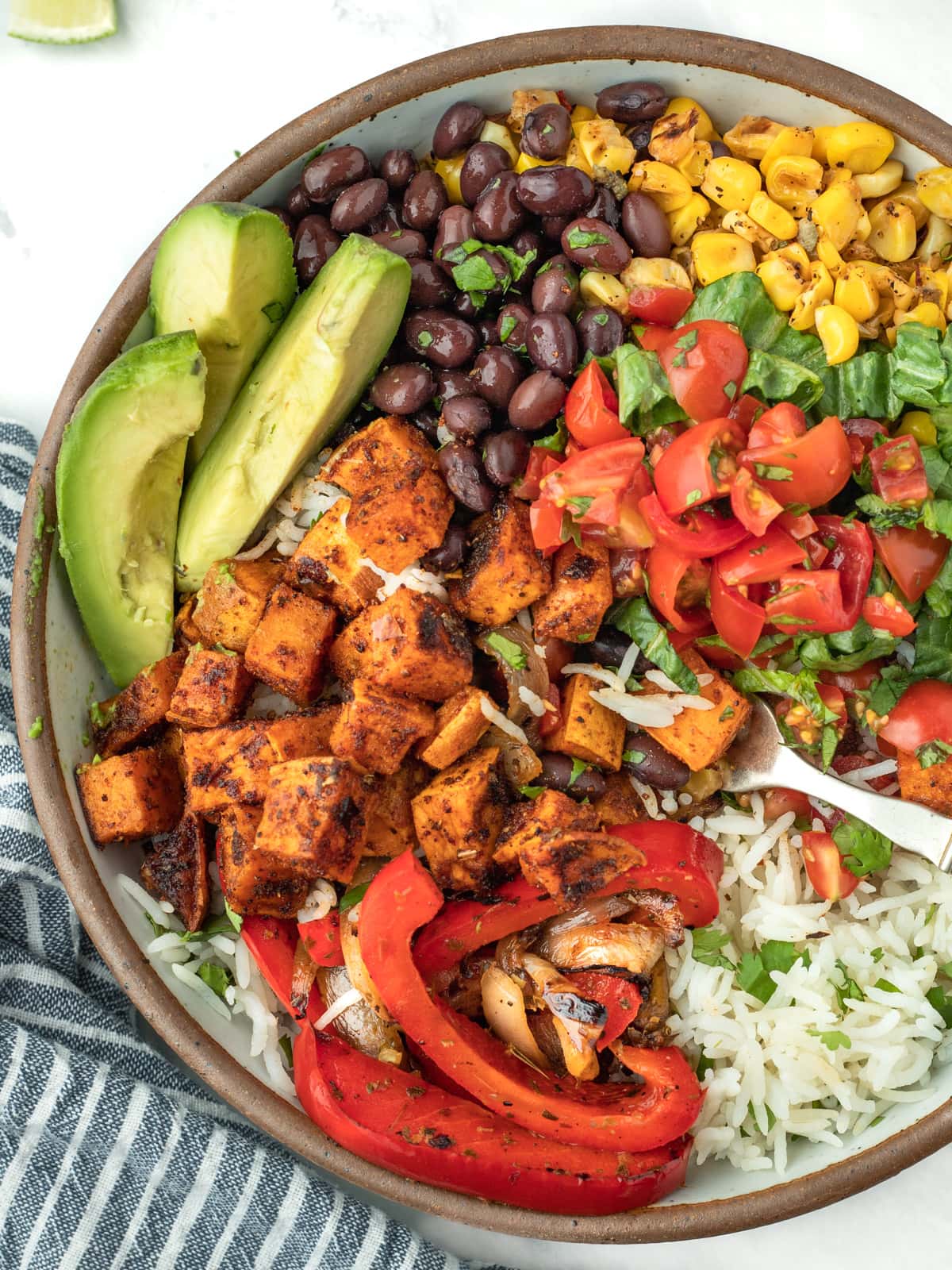 Close up, overhead shot of vegetable burrito bowl with avocados, beans, corn, sweet potatoes, tomatoes and rice.