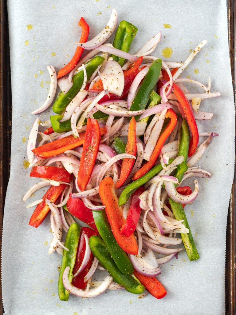 Slices of red and green peppers and red onions on a baking sheet.
