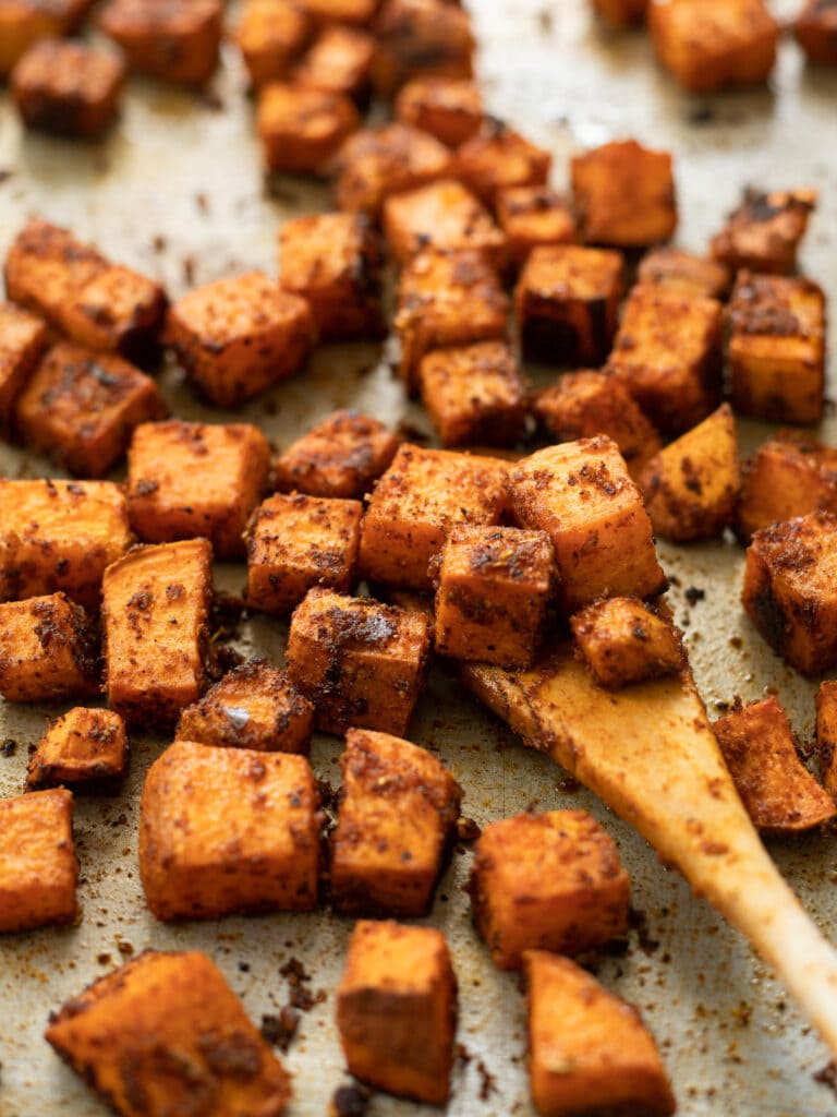 Spicy roasted sweet potatoes being stirred on a baking sheet.