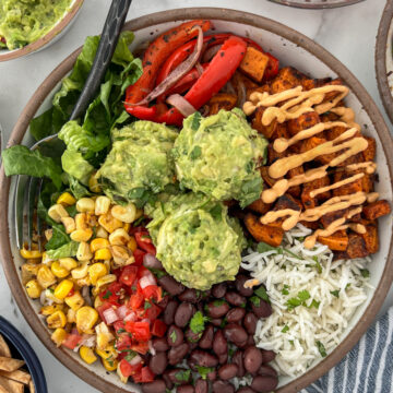 Vegetable burrito bowl with sweet potatoes, red peppers, romain, corn, black beans on a bed of white rice topped with guacamole.