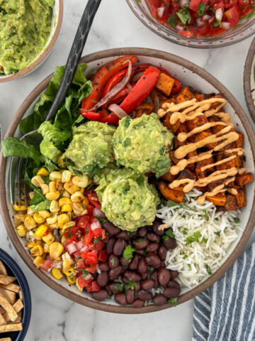 Vegetable burrito bowl with sweet potatoes, red peppers, romain, corn, black beans on a bed of white rice topped with guacamole.