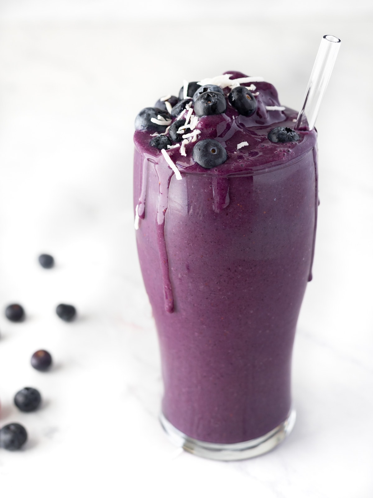 Tall glass of blueberry banana smoothie topped with fresh blueberries and mint.