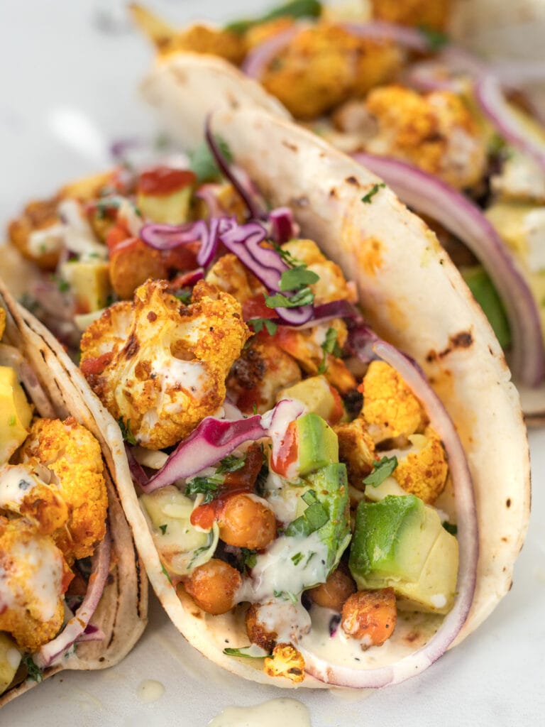 Close up of spicy roasted cauliflower taco with avocado, diced tomatoes, creamy coleslaw and crispy chickpeas.