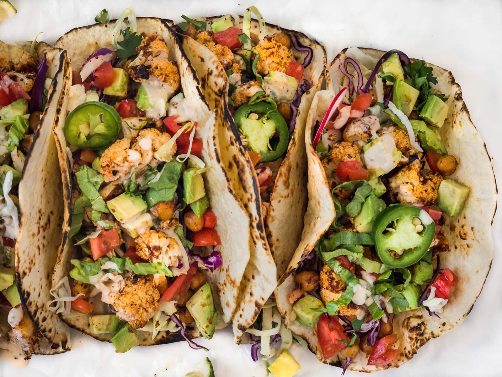 Three large roasted cauliflower and vegetable tacos leaning together on a plate.