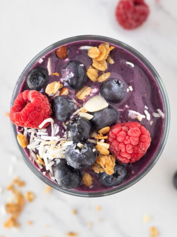 Overhead shot of healthy blueberry banana smoothie topped with fresh blueberries, raspberries and flakes of coconut.