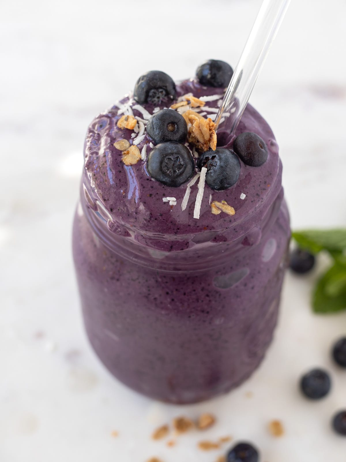 Blueberry banana smoothie in a jar topped with fresh blueberries, granola and shredded coconut.