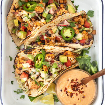 A tray with 3 cauliflower and chickpea tacos served with a bowl of creamy chipotle sauce.