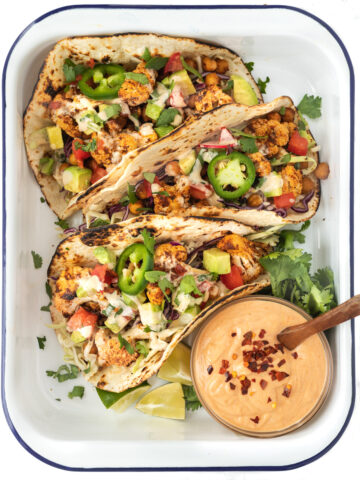A tray with 3 cauliflower and chickpea tacos served with a bowl of creamy chipotle sauce.