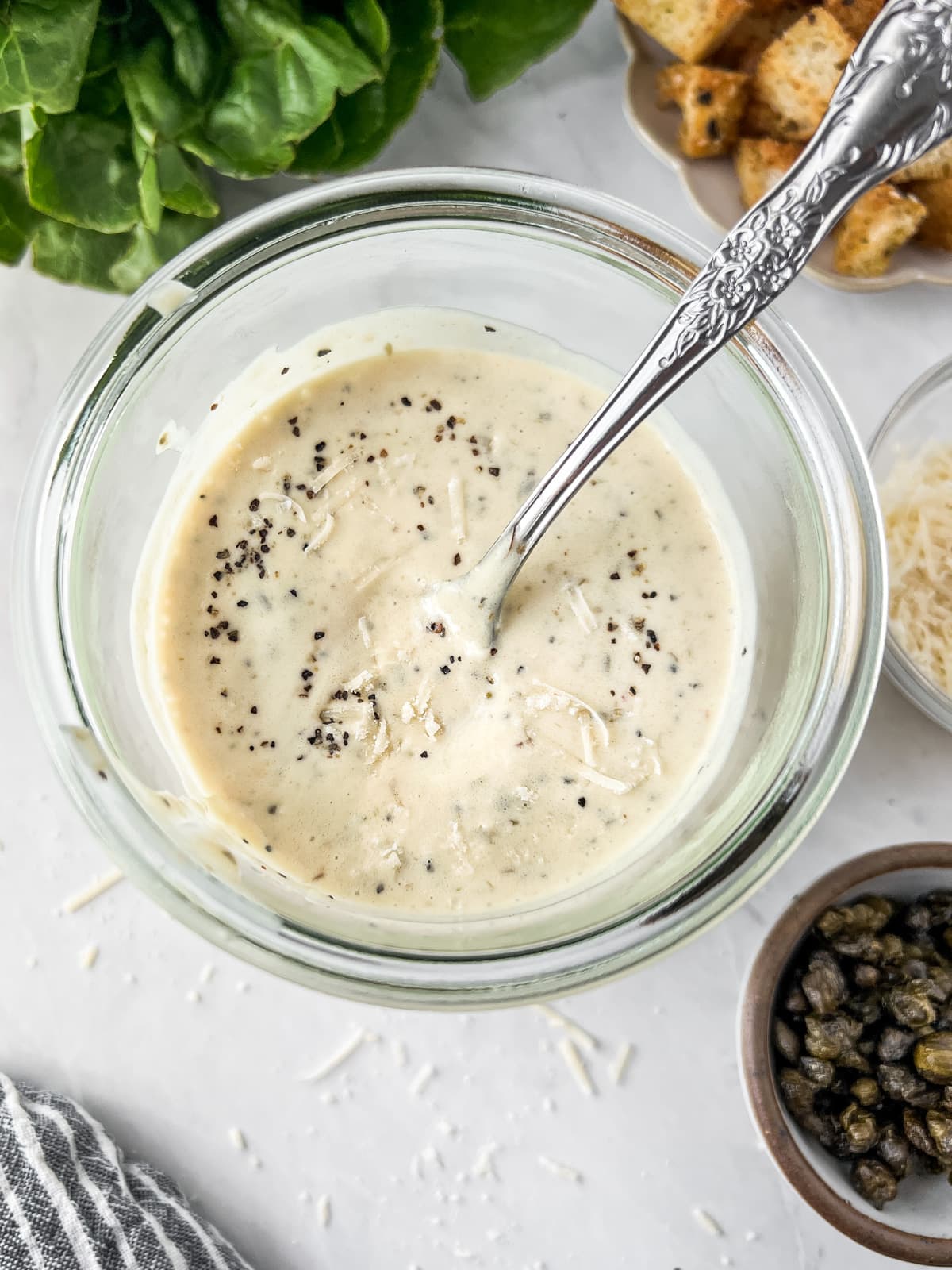 Jar of vegan caesar dressing being stirred with a spoon.