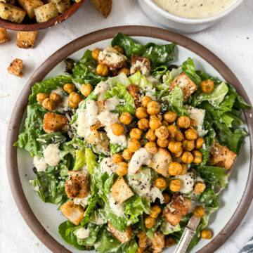 Large plate piled up with caesar salad topped with crispy chickpeas, croutons, dripping with vegan caesar dressing.