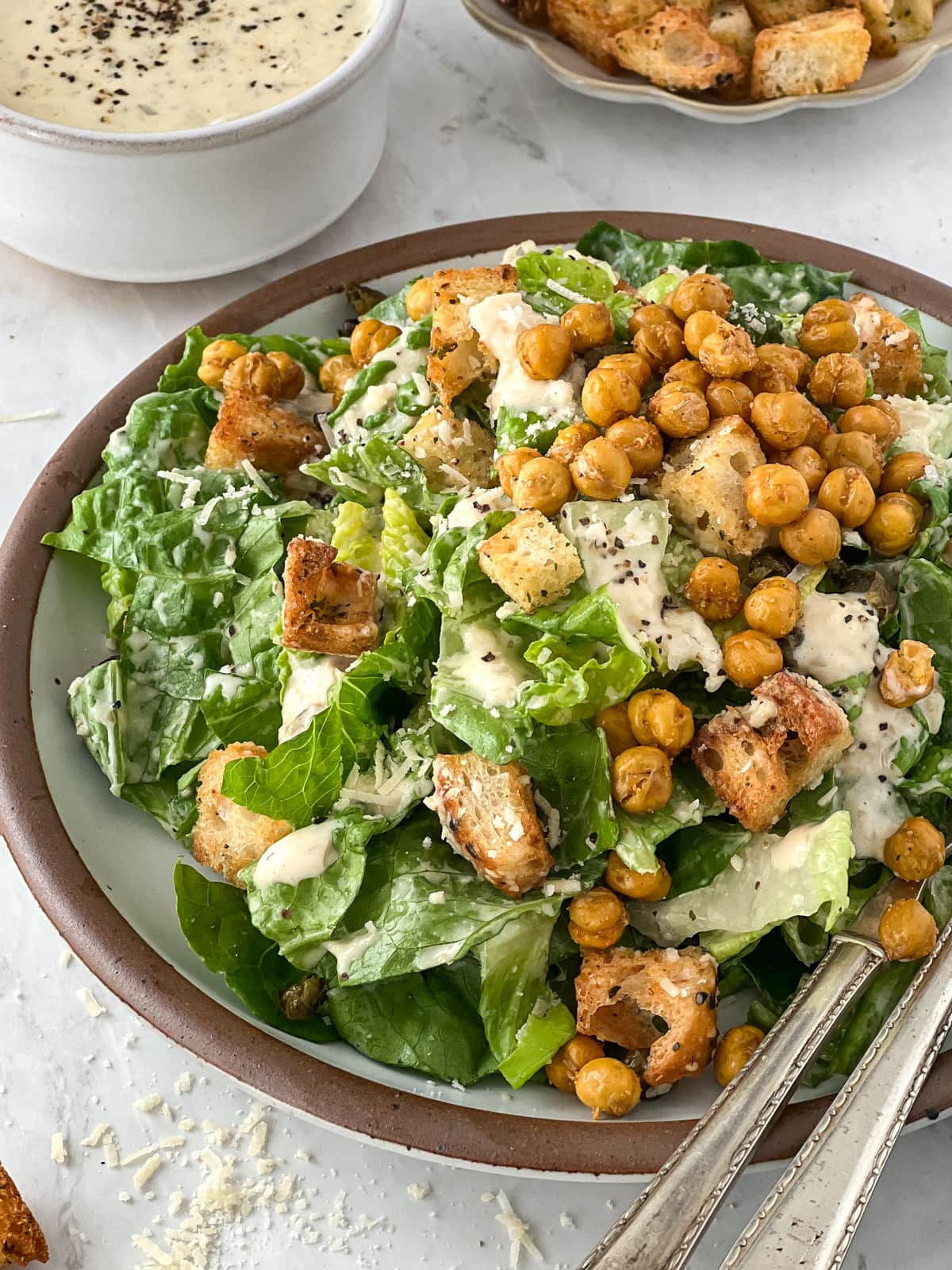 Plateful of caesar salad topped with croutons, crispy chickpeas and dripping with creamy vegan caesar dressing.