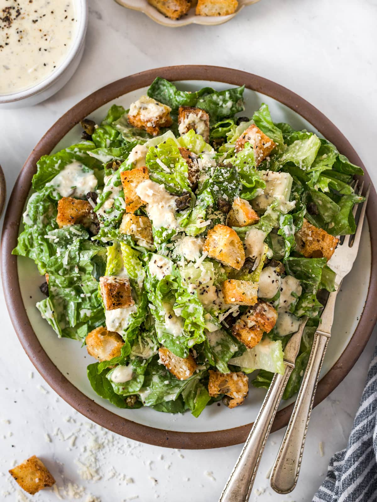 Heaping plate of vegan caesar salad with croutons surrounded by bowls of toppings.
