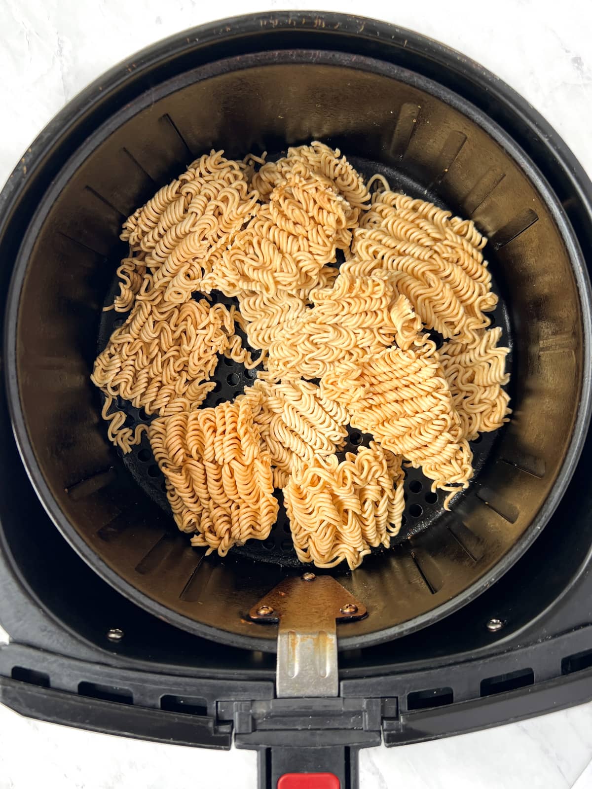 Air fryer basket filled with dry, toasted ramen noodles.