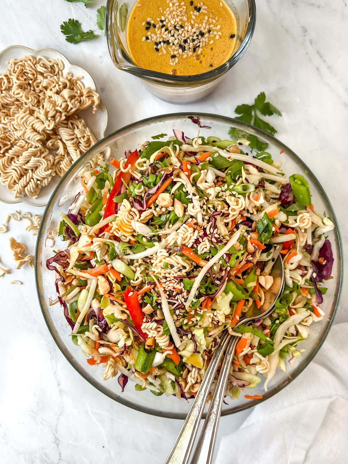 Overhead shot of chopped cabbage salad in a bowl surrounded by ramen noodles and Asian dressing.