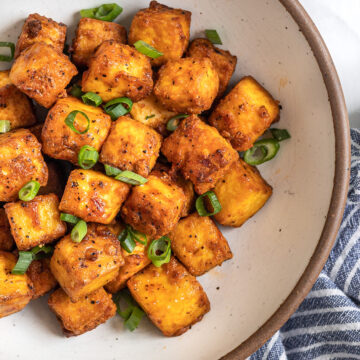 Crispy air fryer tofu on a place with a sprinkle of sliced onions over top.