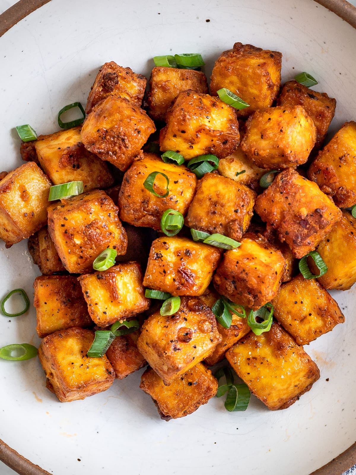 Seasoned crispy tofu piled on a plate with a sprinkle of sliced onions.