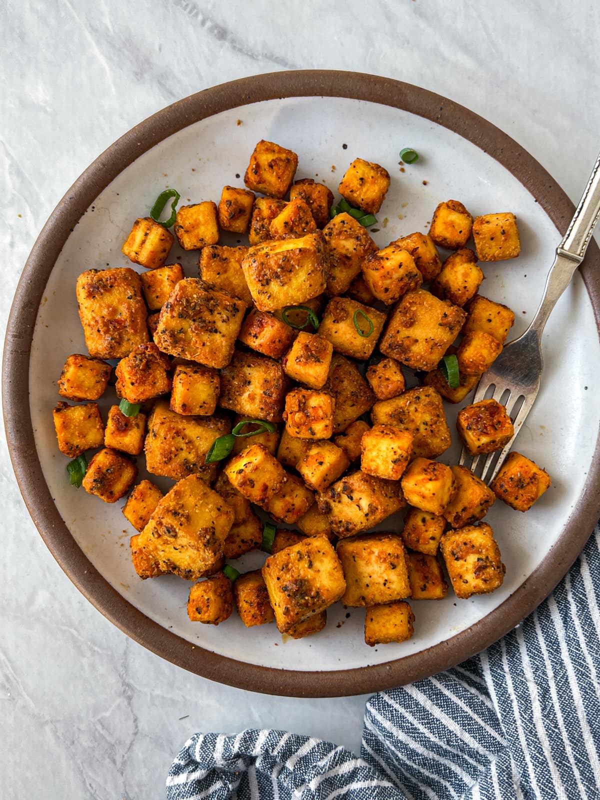 Plate covered in crispy tofu cubes with a silver fork.