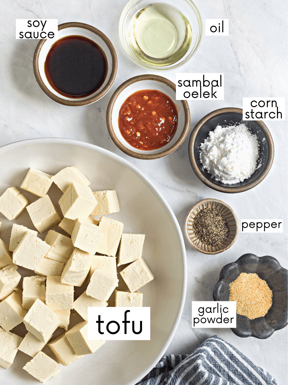 Bowlful of extra firm tofu cubes surrounded by tofu marinade ingredients in individual dishes. 
