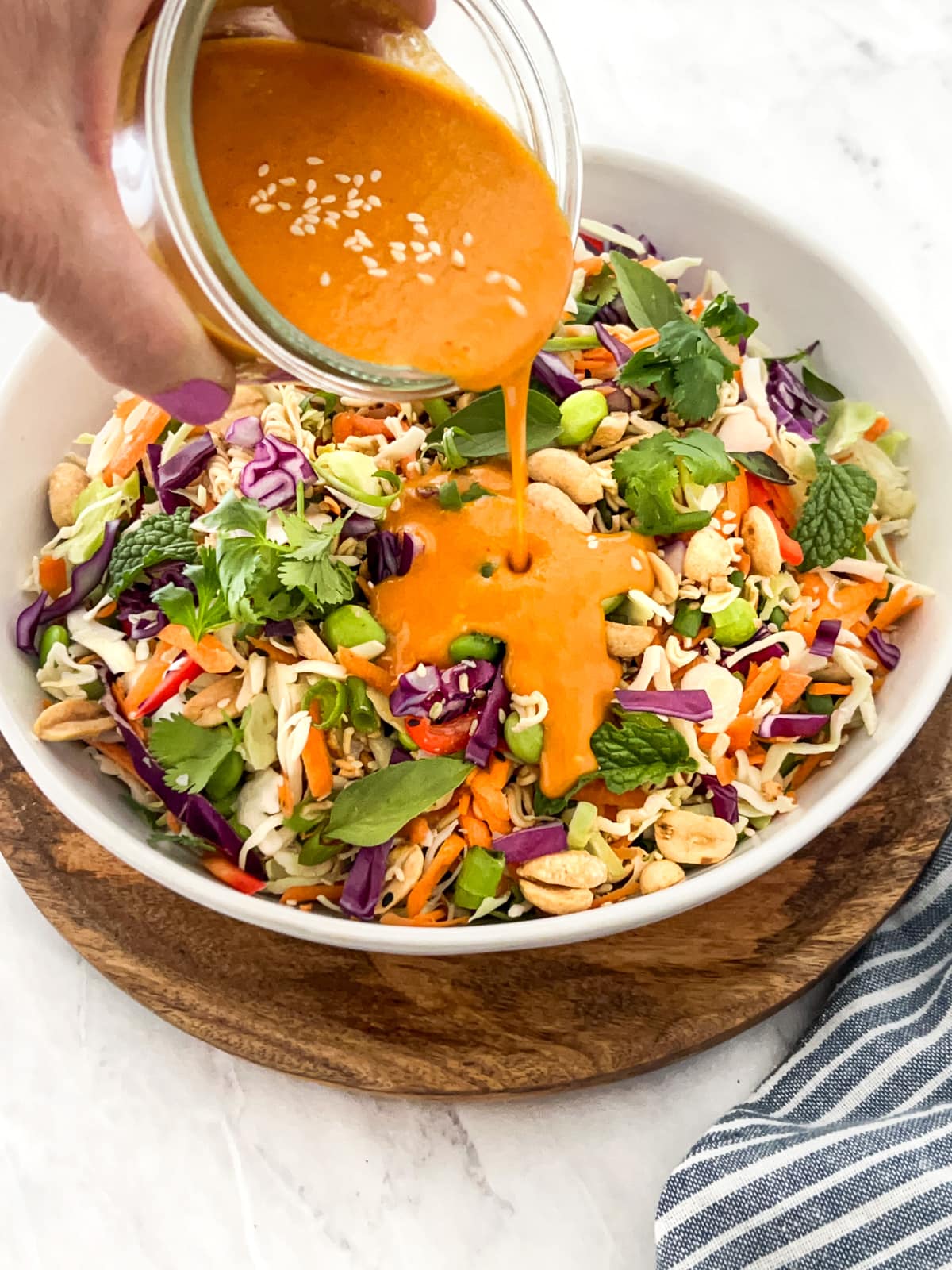 Asian carrot ginger dressing being poured over a bowl of slaw.
