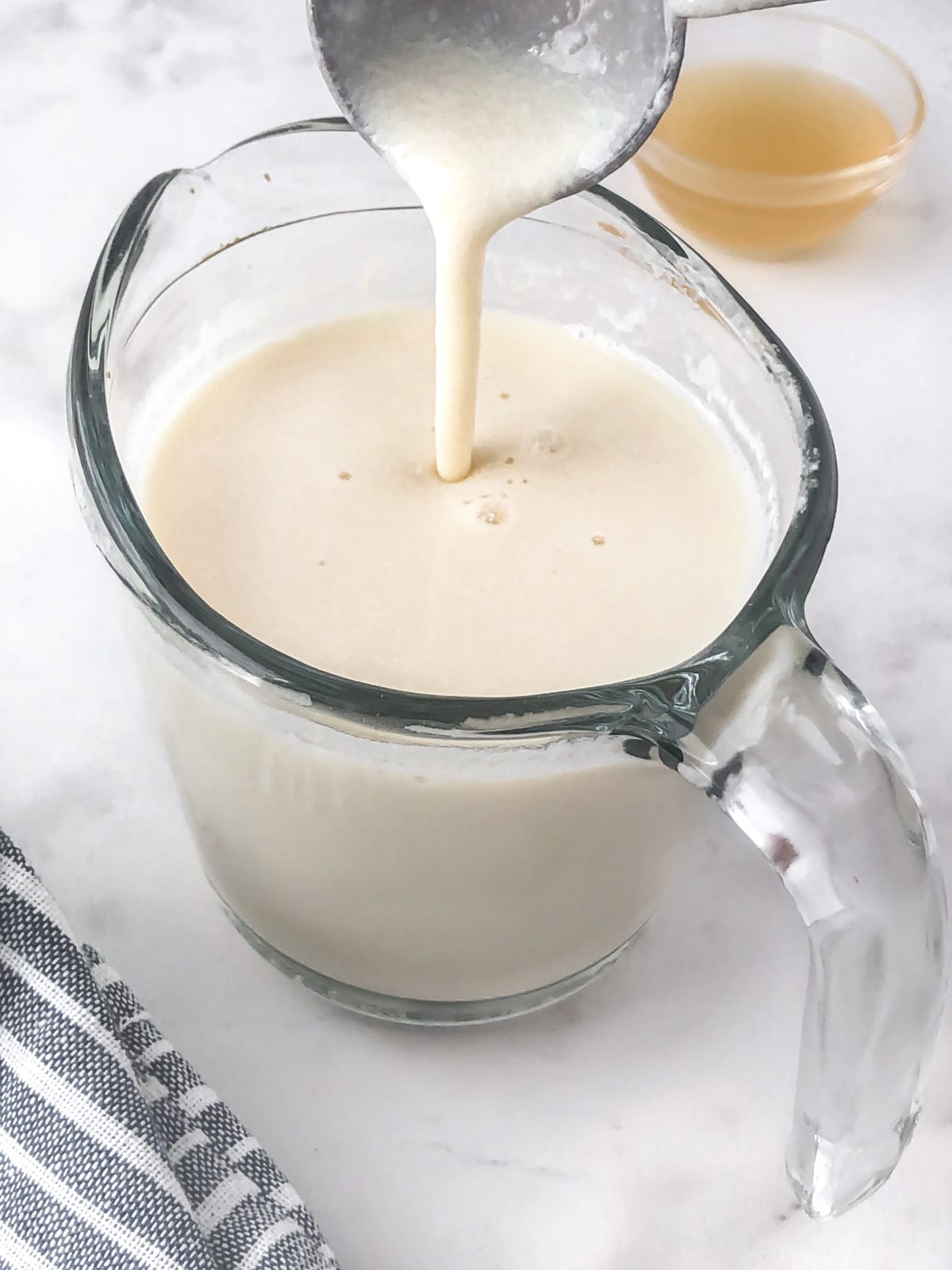 Vegan buttermilk in a measuring cup being stirred with a measuring spoon.