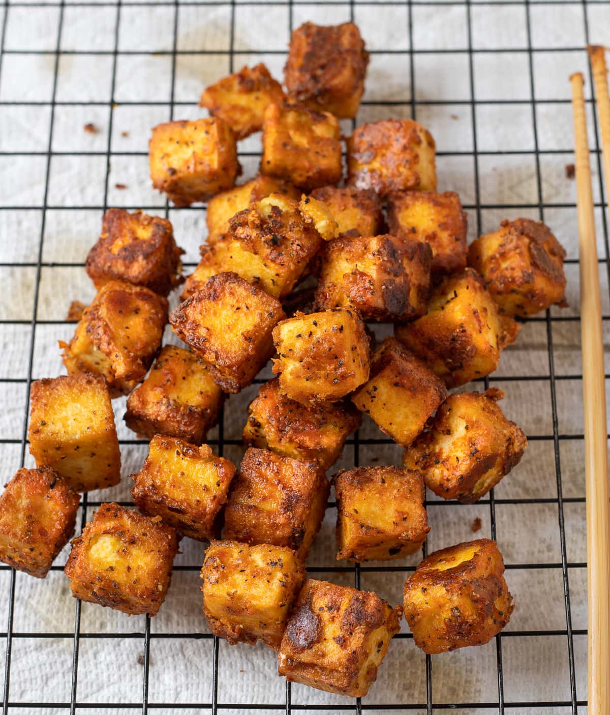 Crispy pan-fried tofu draining on a rack over paper towels.