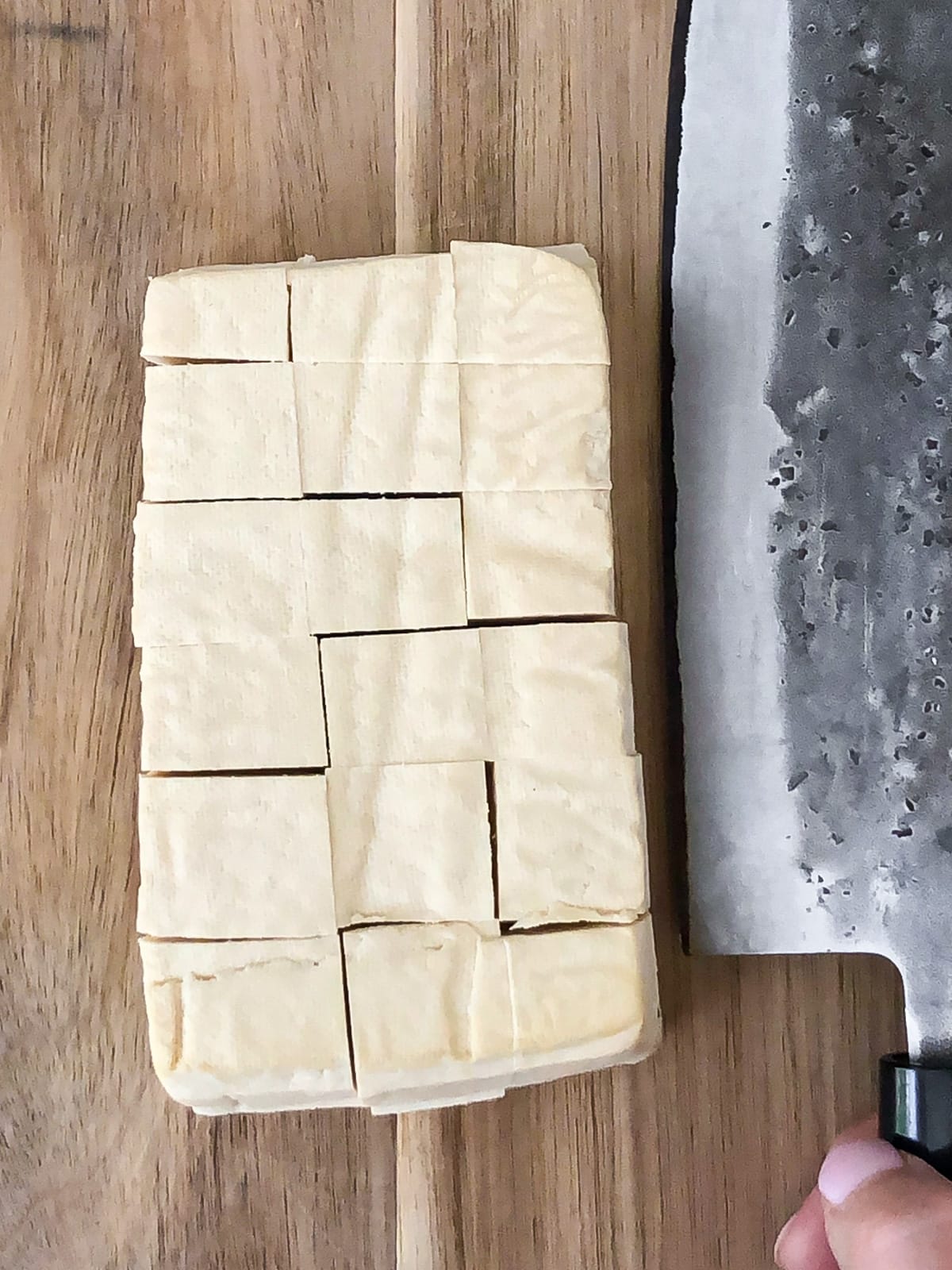 A block of tofu cut into a grid of cubes sitting on a cutting board.