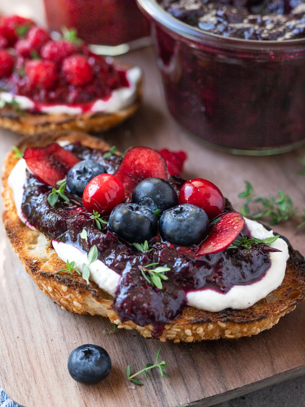Sourdough toast piled high with vegan cream cheese, mixed berry jam, and fresh berries on top.