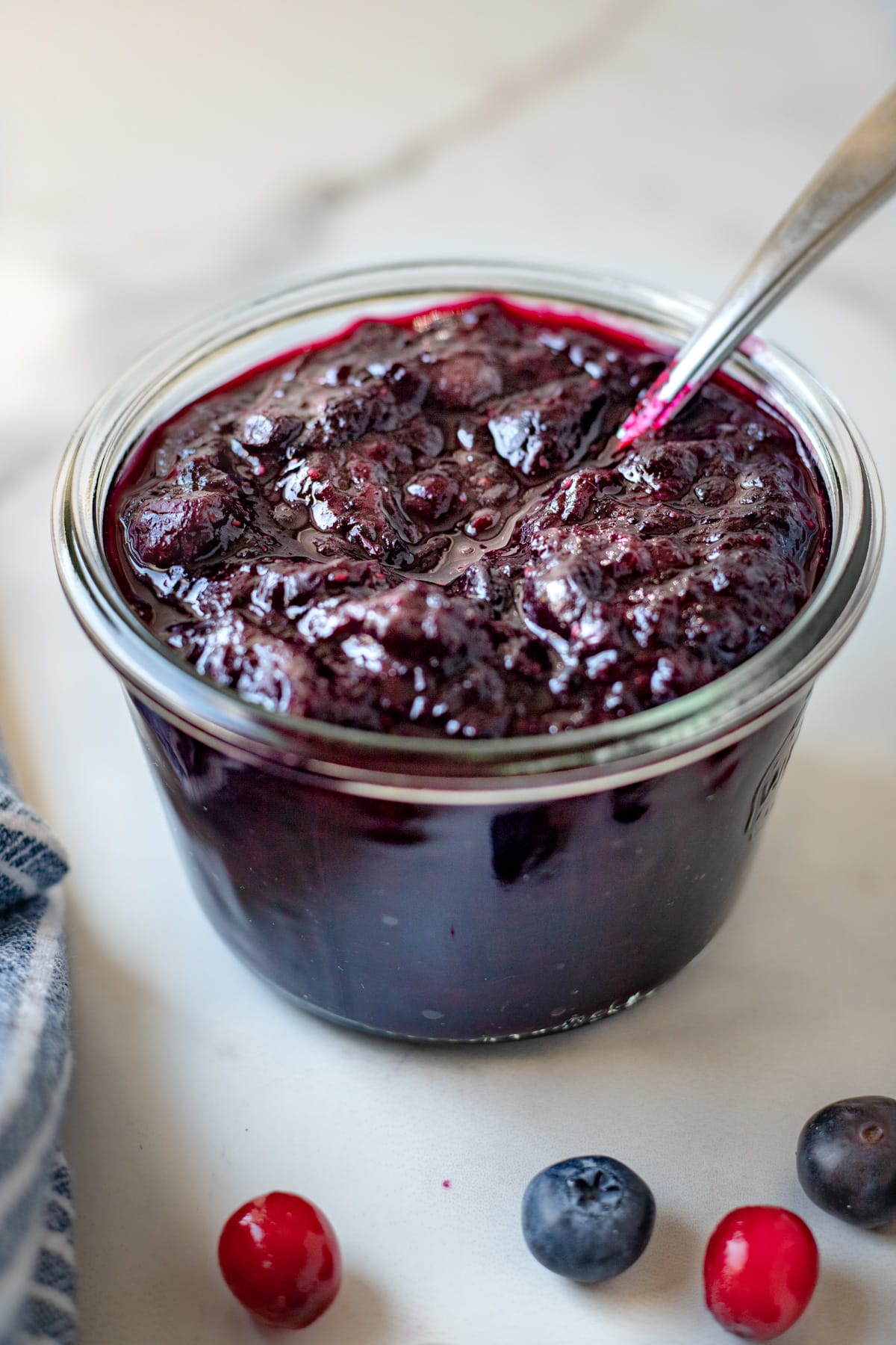 Cherry jam in a weck jar surrounded by fresh berries.