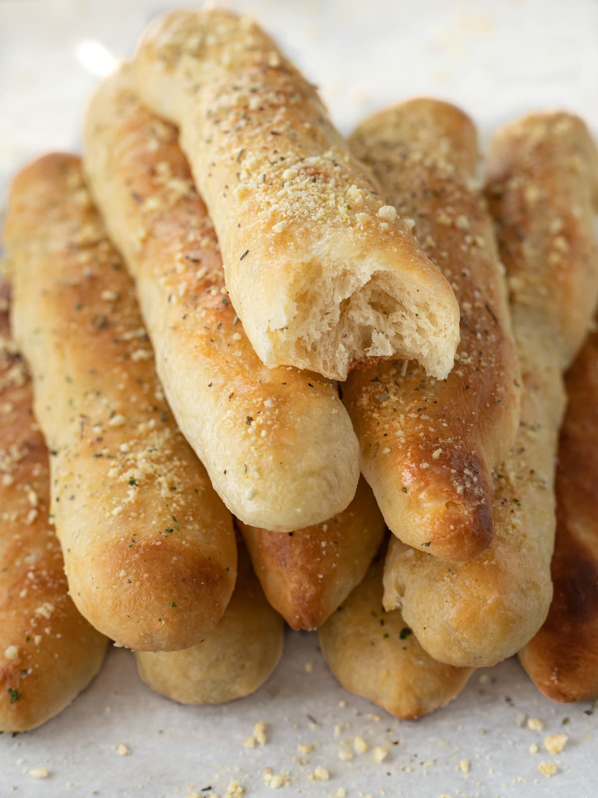 Many golden parmesan cheese breadsticks piled on a baking sheet.