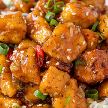 Close up of crispy pan fried tofu in orange sauce served on rice.