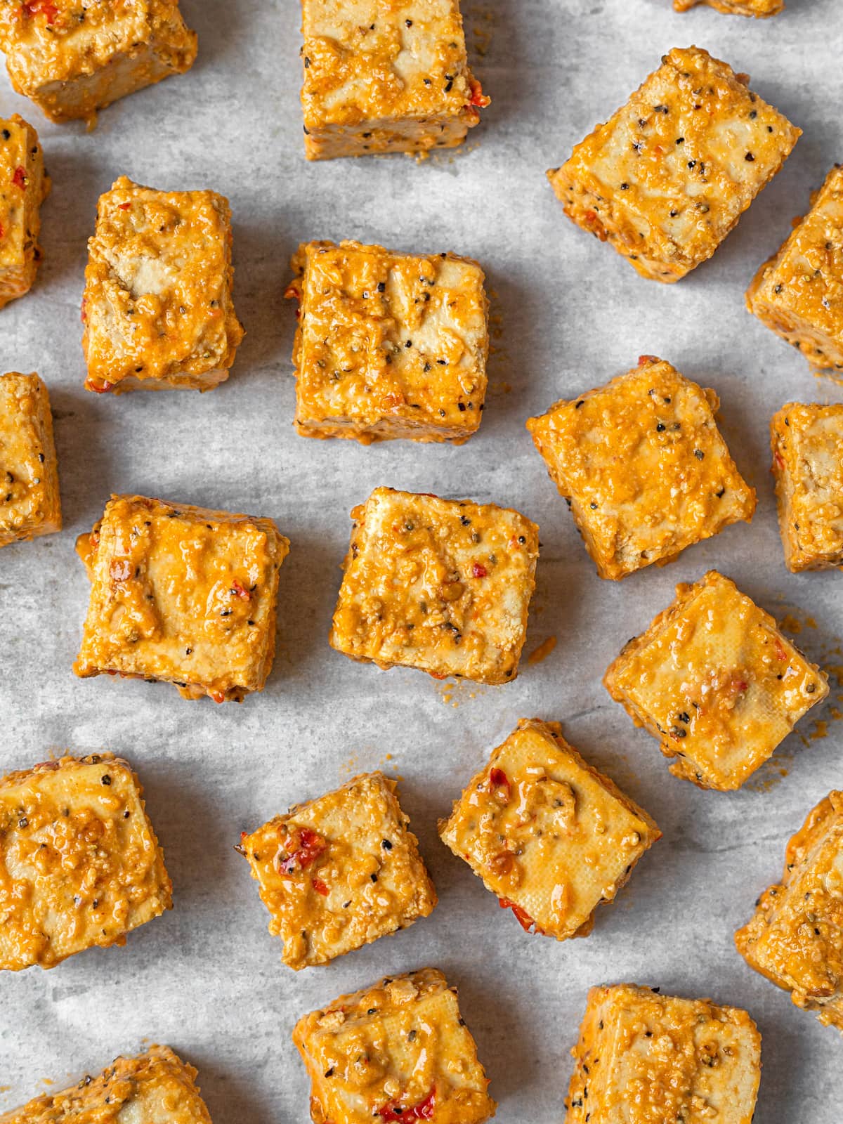 Cubes of seasoned, marinated tofu on a baking sheet ready for baking.