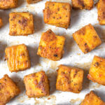 Baked tofu cubes on a parchment paper lined cookie sheet.