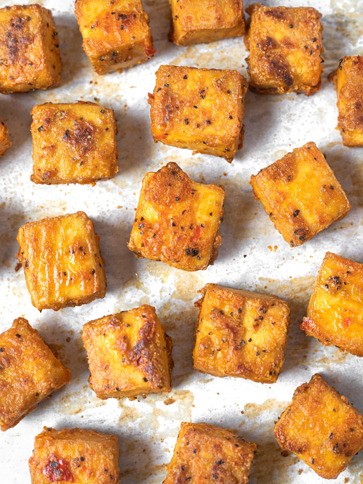 Baked tofu cubes on a parchment paper lined cookie sheet.