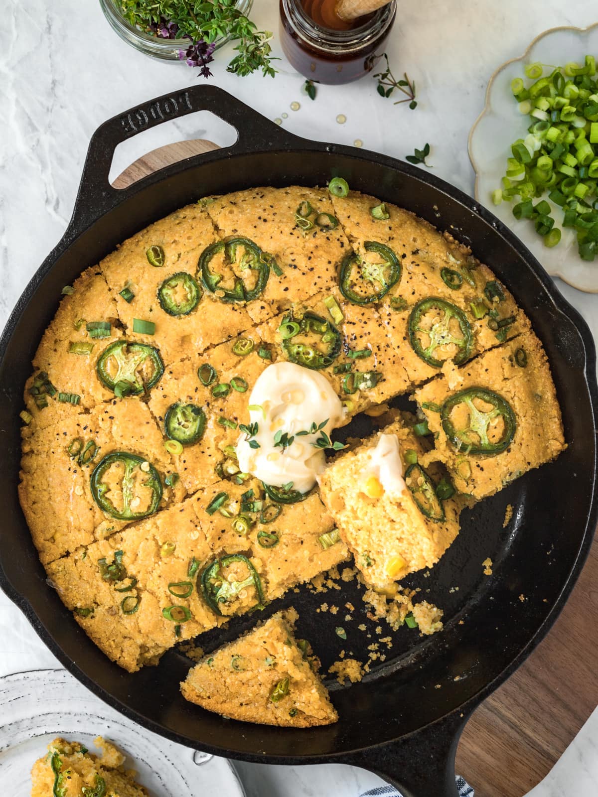 Homemade jalapeno cornbread in a cast iron skillet topped with butter and honey.