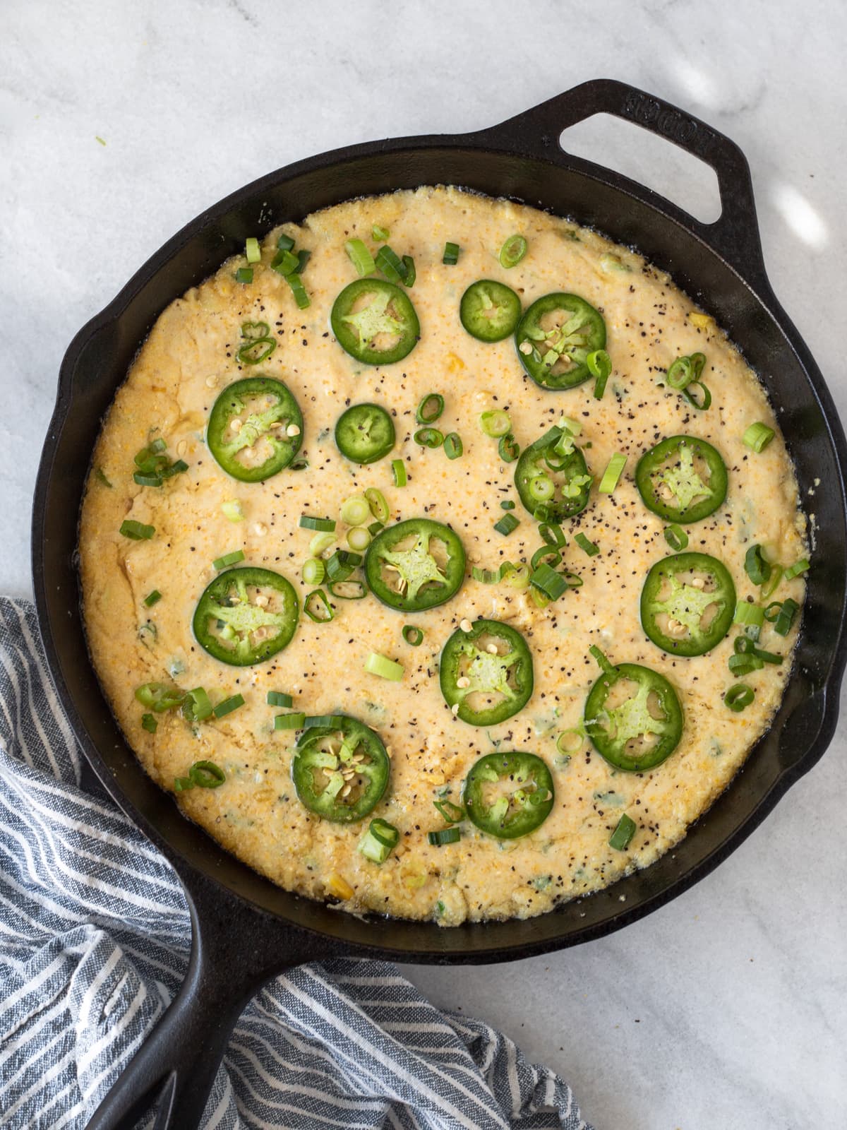 Cornbread batter topped with slices of jalapenos and green onions in a cast iron skillet.