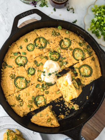 Stone ground cornbread in a cast iron pan topped with jalapenos and whipped butter.