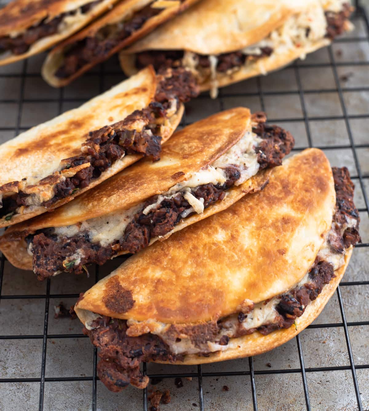 Stack of crispy black bean and cheese tacos on a cooling rack.