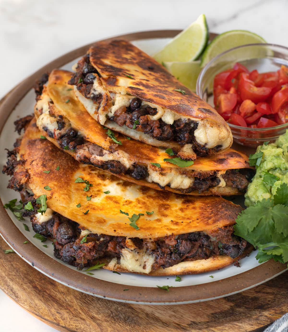 Black bean and cheese tacos stacked on a plate with guacamole.