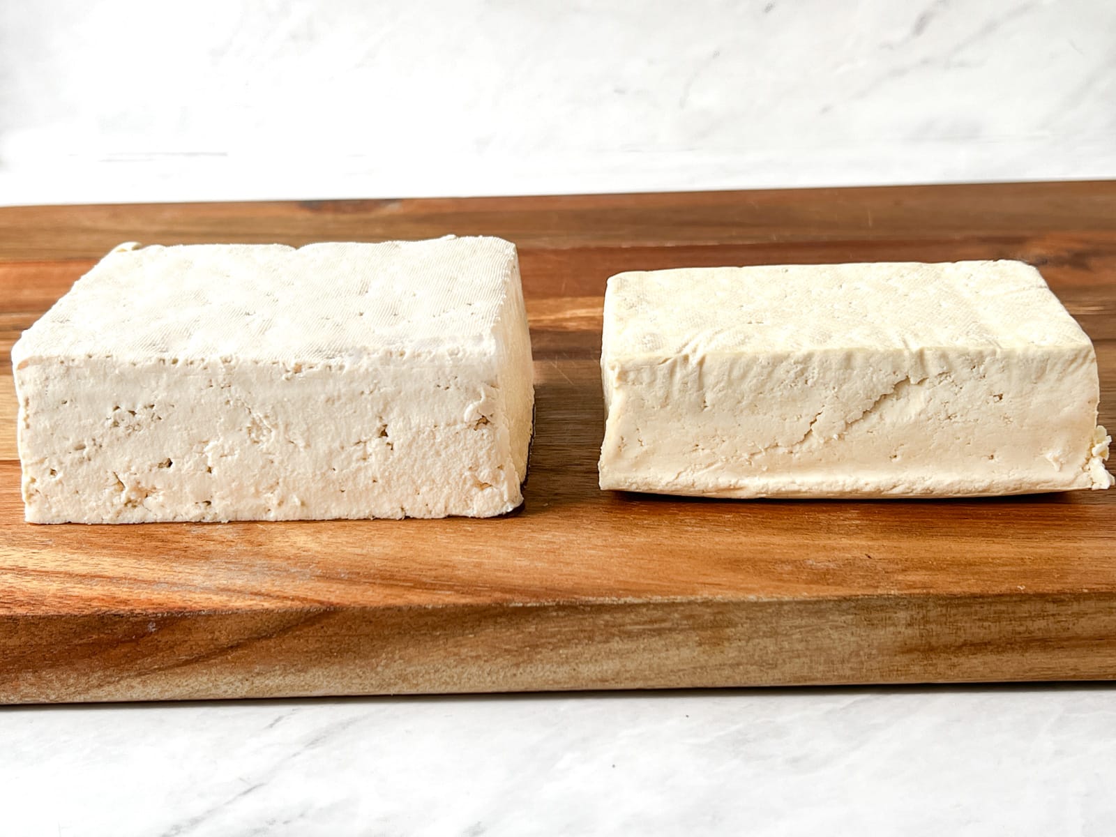 Two blocks of raw tofu on a cutting board.